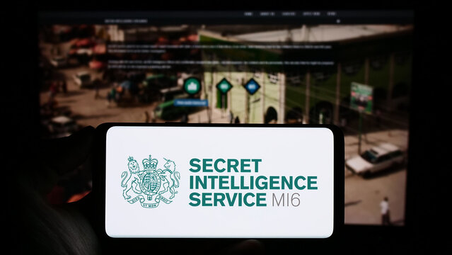 Stuttgart, Germany - 11-12-2023: Person holding cellphone with seal of British agency Secret Intelligence Service (SIS, MI6) in front of webpage. Focus on phone display.