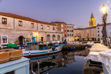 Evening atmosphere in the old harbour of Muggia, a coastal town near Trieste in northern Italy with moored small motor boats. - obrazy, fototapety, plakaty