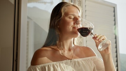Closeup portrait of young woman with closed eyes enjoying taste of red wine in sunset light