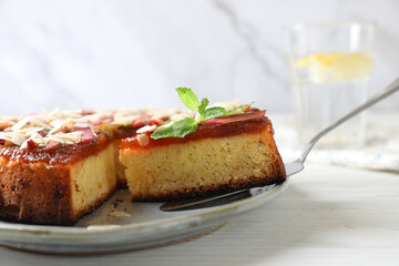 Taking piece of freshly baked rhubarb pie with almond flakes on white wooden table, closeup