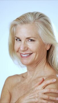 Vertical video portrait of happy pretty mature woman touching shoulder and smiling looking at camera. Advertising of body care spa procedures concept.