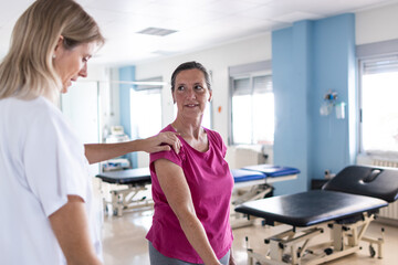 The middle aged female patient is in the rehabilitation gym while her physical therapist teaches her how to do some exercises.