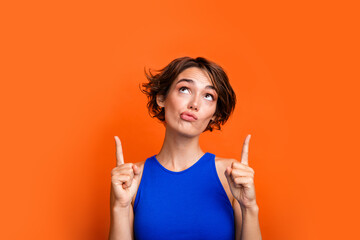 Photo of doubtful unsure girl dressed blue top looking showing two fingers up empty space isolated orange color background