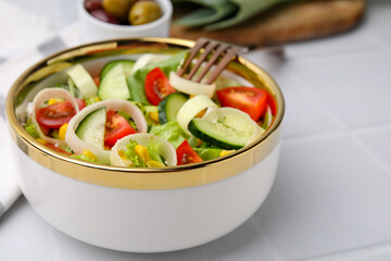 Bowl of tasty salad with leek, tomatoes and cucumbers on white tiled table, closeup