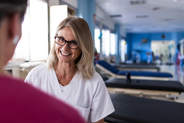 Blonde nurse with glasses is talking to her patient sitting in front of her.