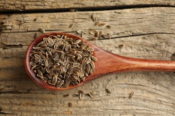 Fototapeta na wymiar Spoon of dry dill seeds on wooden table, top view