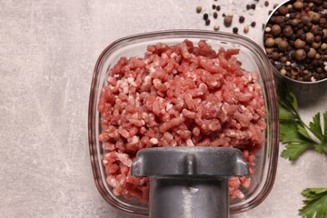 Manual meat grinder with beef mince, peppercorns and parsley on light grey table, flat lay
