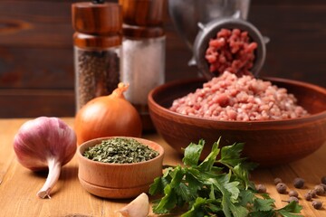 Manual meat grinder with beef mince, spices and parsley on wooden table, selective focus