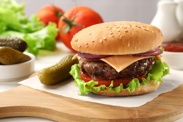 Tasty hamburger with patty, cheese and vegetables served on table, closeup
