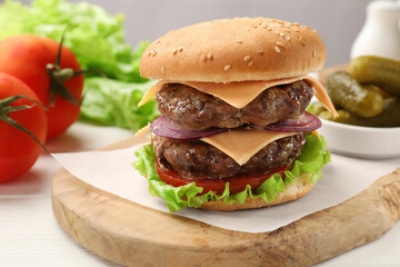 Tasty hamburger with patties, cheese and vegetables on table