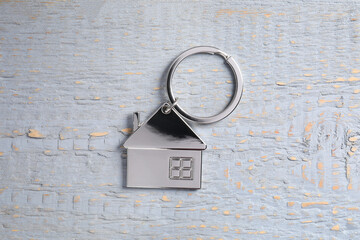 Metal keychain in shape of house on grey wooden table, top view