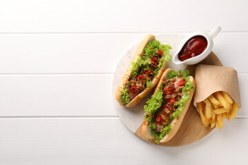 Tasty hot dogs with chili, lettuce, ketchup and French fries on white wooden table, top view. Space...
