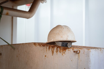 The dirty white safety helmet of hardhat for construction worker, that placed on the metal part....