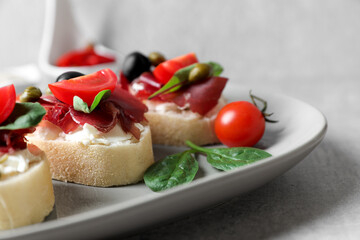 Delicious sandwiches with bresaola, cream cheese, olives and tomato on light grey table, closeup
