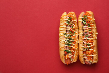 Delicious hot dogs with bacon, carrot and parsley on red background, top view. Space for text