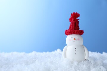 Cute decorative snowman on artificial snow against light blue background, space for text