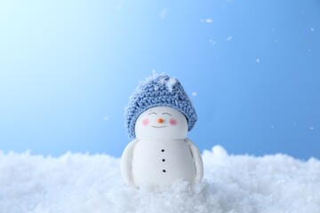 Cute decorative snowman on artificial snow against light blue background
