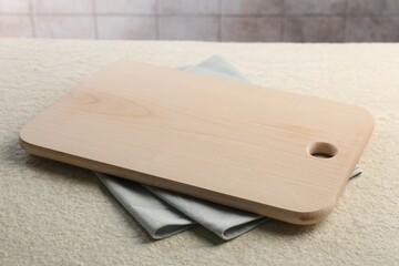 Wooden cutting board and napkin on beige table, closeup