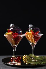 Creative presentation of Christmas Sangria cocktail in baubles and glasses on grey table against black background
