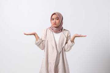 Portrait of confused Asian hijab woman in casual suit spreading hands sideways, feeling doubt while making choice. Businesswoman concept. Isolated image on white background