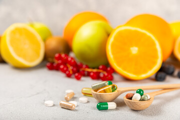 Vitamins and supplements. Variety of vitamin tablets in a wooden spoon on a texture background.Multivitamins with fresh and healthy fruits.Food supplements. Flat lay. Space for text.Copy space