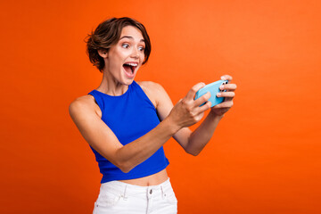 Photo of pretty overjoyed lady hold smart phone have fun playing video games isolated on orange color background