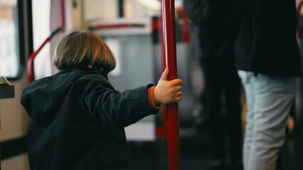 whimsical Little traveler on a train, clutching a metal support bar and twirling around it. A...