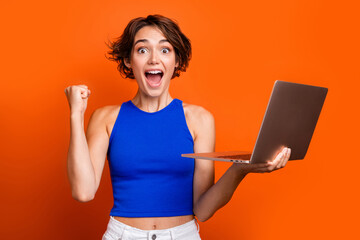 Photo of cute lucky girl dressed blue top rising fist writing emails modern gadget isolated orange color background