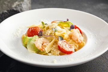 Fettuccine pasta mixed with zucchini ribbons and succulent shrimp, served in a white dish on a dark background, sprinkled with cheese