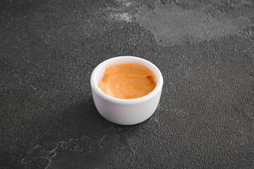 Spicy aioli sauce infused with red pepper presented in a white dipping bowl on a sleek black...