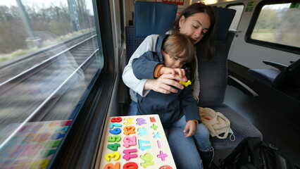 Proactive mom facilitating an educational activity for her son during a fast train commute, exemplifying on-the-move childhood learning
