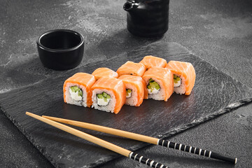 Philadelphia sushi roll with fresh salmon and cucumber, elegantly presented on a black slate board,...
