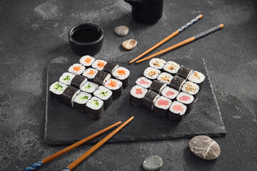 Obraz na płótnie Canvas A classic assortment of hosomaki sushi featuring salmon, tuna, cucumber, and eel, beautifully arranged on a black slate with soy sauce.
