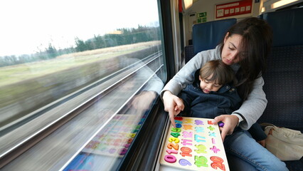 Proactive mom facilitating an educational activity for her son during a fast train commute,...