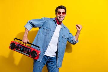 Photo portrait of nice young man dancing hold boom box excited wear trendy jeans garment isolated on yellow color background