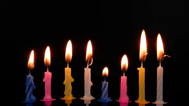 Colorful cake birthday candles burning on black background.