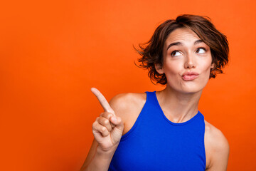 Photo of thoughtful adorable girl dressed blue top looking pointing finger empty space isolated orange color background