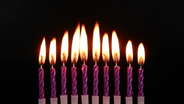 Ten purple birthday candles burning on black background.	