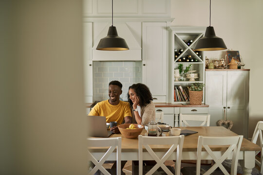 Smiling young multiethnic couple using a laptop during breakfast at home