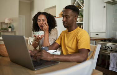 Young multiethnic couple working on a laptop during breakfast at home