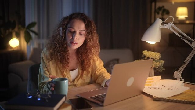 Focused young woman freelancer at night with cup of hot coffee for effective working at desk indoors Concentrated female with late work drinking caffeine for extra energy at home workplace Deadline