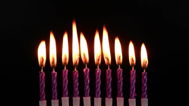 Ten purple birthday candles burning on black background.