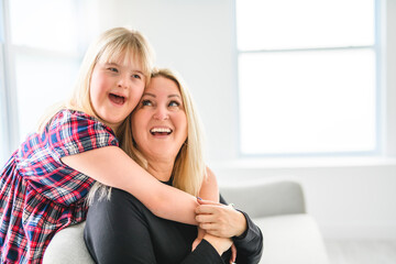 Mother and sweet down syndrome daughter girl at home sofa