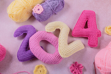 New Years background 2024. Multicolored crochet numbers, skein of wool yarn and knitting needles on gray background. New Years start creative handcrafted idea for DIY crafters