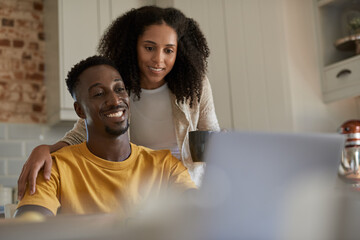 Smiling young multiethnic couple using a laptop together in their kitchen - Powered by Adobe