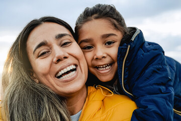 Happy Latina mother and child daughter having fun in winter time outdoors. Family love and travel vacations - obrazy, fototapety, plakaty
