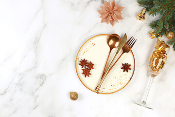 Christmas table setting. Festive New Year's cutlery with a napkin on a plate on a marble concrete background, festive composition with fir branches and a glass of champagne, kitchen background.