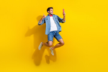 Full size photo of cool guy wear jeans jacket scarf jumping doing selfie show thumb up on...