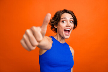 Photo of cute astonished girl open mouth demonstrate thumb up confirmation isolated on orange color...