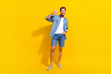 Full size photo of satisfied guy wear jeans jacket shorts arm in pocket show thumb up nice work isolated on bright yellow color background